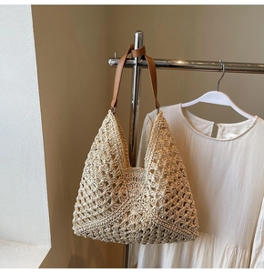 Close-up of beige hollow woven straw tote bag with brown leather straps hanging naturally