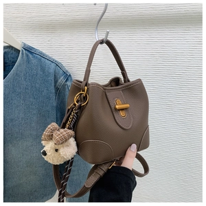Detailed close-up of brown litchi pattern leather bucket bag with gold lock and bear charm
