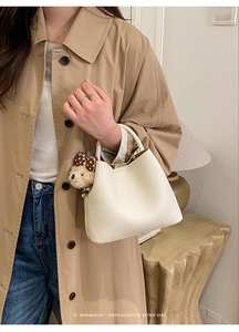 Detail of cream bucket bag with litchi texture and cute brown plush bear charm