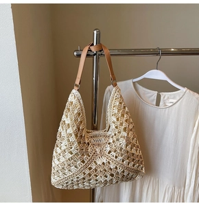 Detail of hand-woven straw tote bag with brown leather strap hanging next to a white dress