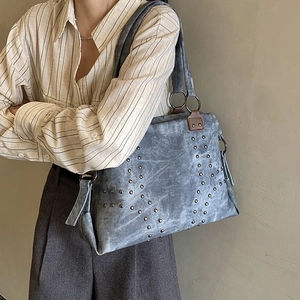 Détail du sac cabas gris-bleu avec rivets, poignées en cuir et pompon à fermeture