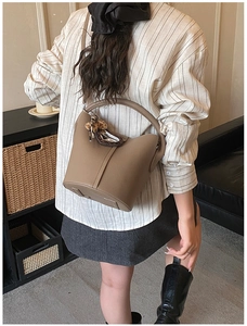 Détail d'un sac seau en cuir marron avec un foulard léopard noué sur la poignée