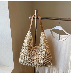 Detail of hollow floral crochet pattern on beige straw tote bag with brown leather strap