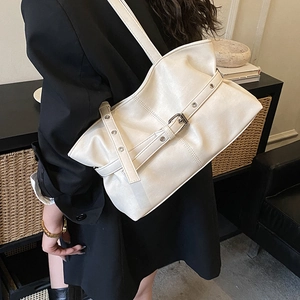 Détail du grand sac bandoulière crème avec boucles argentées sur une veste de blazer noire