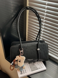 Minimalist black vintage shoulder bag with plush bear charm on a design book background