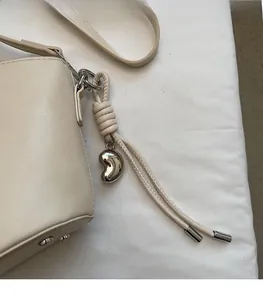Vue détaillée du sac crème présentant un pendentif en métal argenté en forme de haricot