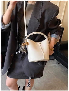 Gros plan du sac seau beige texture litchi porté par un mannequin en blazer gris