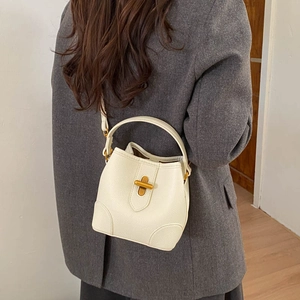Lifestyle view of white pebble leather bucket bag with gold cross-lock and strap