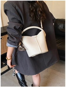 Détail d'un sac seau crème avec texture litchi porté par un mannequin en costume chic