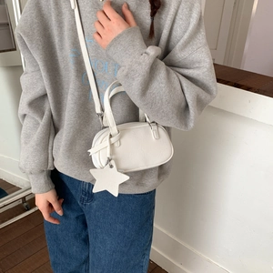 Close-up of a white leather Boston bag with star charm worn by a model in casual style