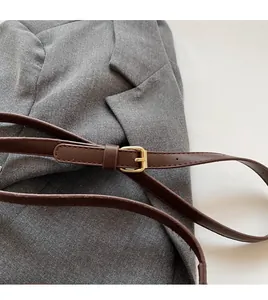 Detail of dark brown leather strap with polished gold buckle on a gray blazer background
