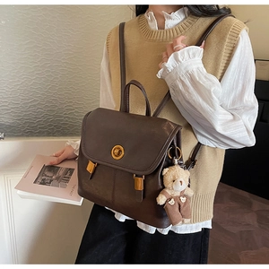 Close-up of vintage dark brown leather backpack with gold clasp and cute bear charm pendant