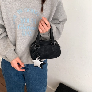 Close-up of black Boston bag with star pendants and ribbon on textured background