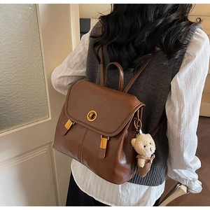 Detail view of vintage brown leather backpack featuring a gold clasp and cute bear charm