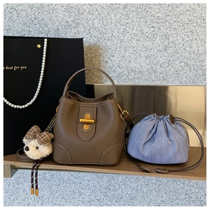 Brown bucket bag with gold clasp, striped inner pouch and plush bear charm on a shelf