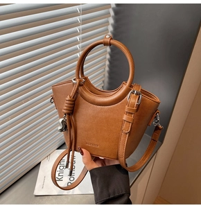 Détail du sac seau en cuir marron avec poignées rondes rigides et breloque coeur