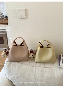 Detailed close-up of minimalist leather bucket bags in pink and yellow with teddy bear charms