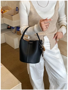 Détail d'un sac seau en cuir noir grainé avec des lignes verticales et un charme léopard