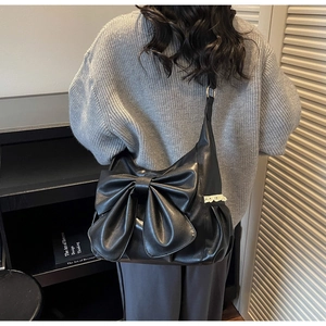 Detail view of black faux leather shoulder bag with a large 3D bow and white lace accents
