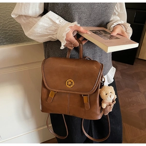 Detail of vintage brown leather backpack featuring a gold twist lock and cute bear charm