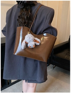 Détail du sac cabas en cuir marron brillant avec un joli lapin en peluche sur la bandoulière