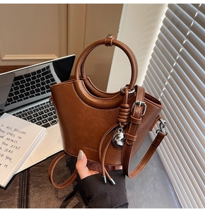 Détail d'un sac seau marron avec poignée ronde, pendentif cœur et pompon sur cuir