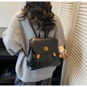 Detail of vintage black leather backpack featuring gold twist lock and cute bear charm