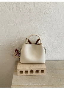 Detail of minimalist cream bucket bag with plush bear charm on a textured stone base