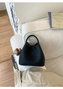 Detail of a black leather bucket bag with a brown plush bear charm in a retro setting