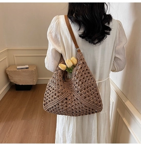 Detail of a large brown crochet tote bag with mesh pattern and leather strap on model