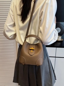 Brown lychee grain leather bucket bag with gold clasp shown on a crossbody model