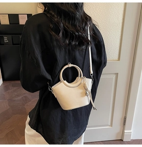 Détail d'un sac seau beige minimaliste montrant la poignée en anneau et le pendentif noué