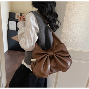Detail of dark brown matte leather shoulder bag with oversized bow and white lace trim