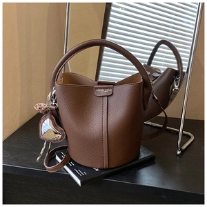 Détail d'un sac seau marron foncé avec texture grainée et breloque en forme de cœur