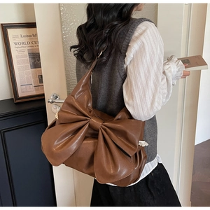 Detail of dark brown shoulder bag featuring a large bow and premium matte leather texture