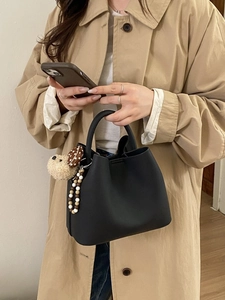 Fashionable black leather bucket handbag with teddy charm held by a model in a trench coat
