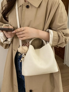 Chic cream white bucket bag with cute charm and adjustable strap worn with trench coat