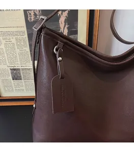 Gros plan du sac bandoulière en cuir marron foncé avec boucle argentée et étiquette de mode