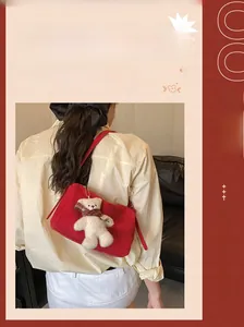 Detail view of red suede pillow bag featuring a plush teddy bear charm and thin shoulder strap