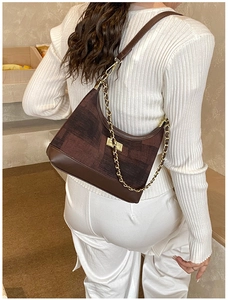 Detail of vintage dumpling bag with textured patterns and gold chain on model shoulder