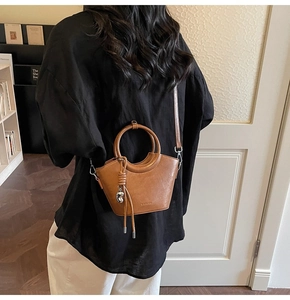 Détail d'un sac seau marron avec poignée ronde en métal et décoration de franges en cuir