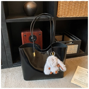 Détail du sac cabas noir brillant avec de longues anses et un pompon en fourrure grise