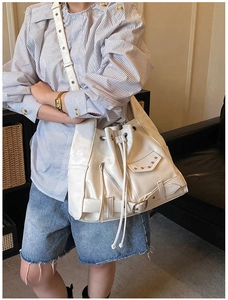 Close-up of white punk style bucket bag with metal rivets and decorative zippers on model