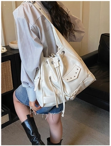 Detailed view of a white studded punk bucket bag with silver rivets worn by a model