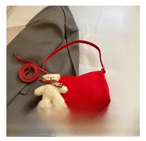 Detail view of red suede shoulder bag featuring a cute white teddy bear plush charm