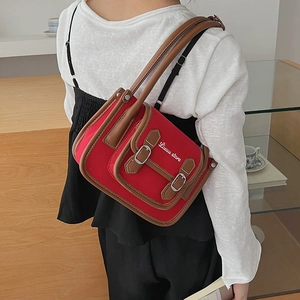 Sac bandoulière en toile rouge avec garniture en cuir brun porté par un mannequin ici
