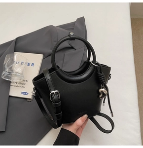 Détail du sac seau noir en cuir avec poignées rondes et pendentif coeur sur blazer gris