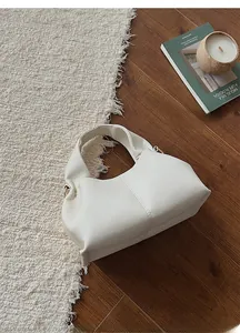 Detail shot of off-white lychee texture leather cloud bag on a rustic wood floor