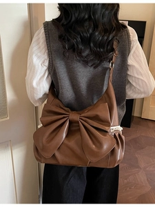 Brown faux leather shoulder bag with a large bow and white lace trim on a model