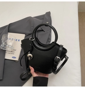 Détail du sac seau noir mat avec poignée ronde et breloque en forme de cœur argenté